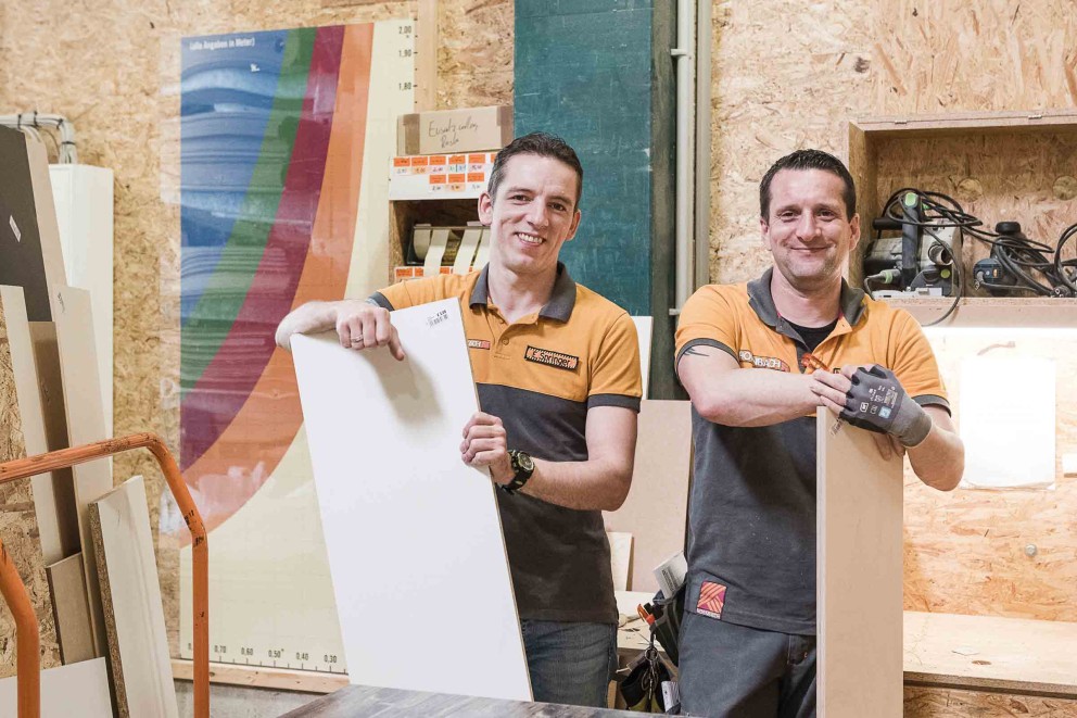Zwei Mitarbeiter präsentieren eine beschichtete Spanplatte im Hornbach-Baumarkt.