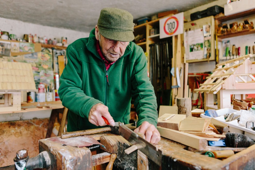 Ein Mann sägt Holz in einer Werkstatt mit Werkzeugen und Holzbauten.
