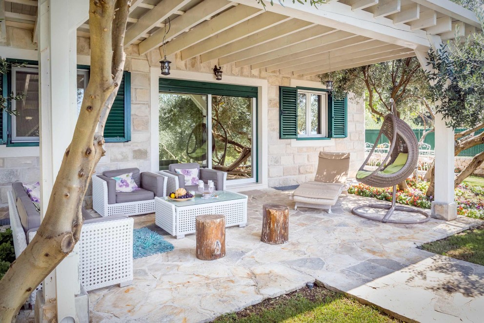 Terrasse avec mobilier de jardin, fauteuils de salon et fauteuil suspendu sous une pergola