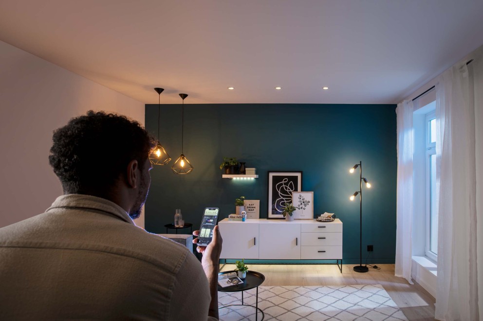 Mann steuert Beleuchtung im Wohnzimmer mit einer App auf seinem Smartphone