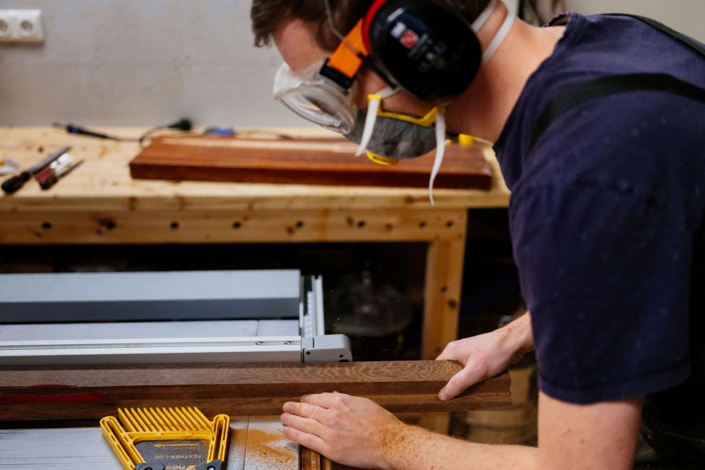 Un homme portant un équipement de sécurité coupe une planche de bois avec une scie à table