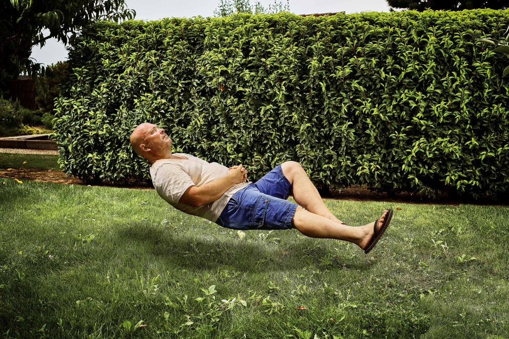 Mann entspannt auf Rasen vor geschnittener Hecke