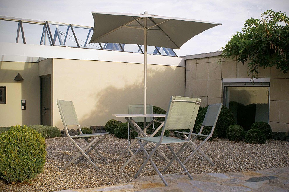 Gartenszene mit Gartentisch, Gartenstühlen und Sonnenschirm auf Kiesboden