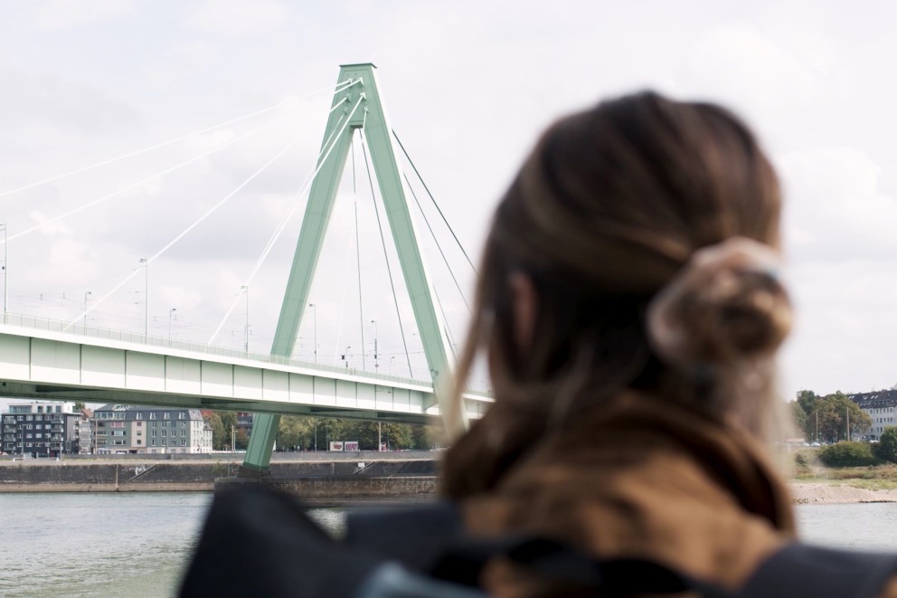 
				Anna admire un pont en acier au bord du Rhin.

			