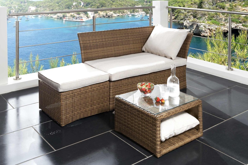 Terrasse mit Rattanmöbeln, bestehend aus Bank, Hocker und Tisch mit Glasplatte