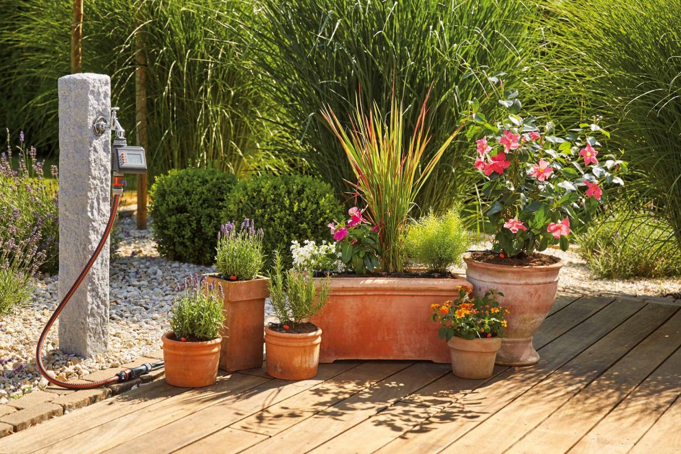 Gartenbewässerungssystem mit Wasserhahn, Schlauch und verschiedenen Blumen in Tontöpfen auf einer Holzterrasse