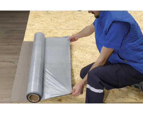 Une personne déroule un film de construction sur une surface en bois.