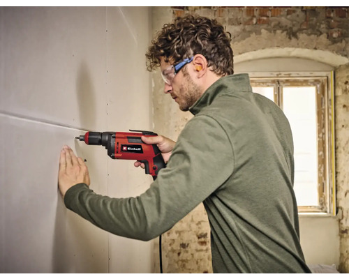 Un homme perce un trou dans un mur avec une perceuse Einhell.
