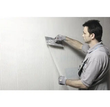 Un homme applique de la colle sur un mur à l''aide d''une truelle.