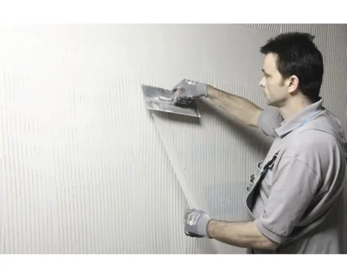 Ein Mann trägt mit einer Kelle Klebstoff auf eine Wand auf.