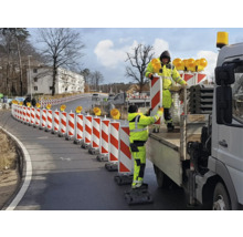 Bauarbeiter stellen eine rot-weisse Verkehrsleiteinrichtung mit Warnleuchten auf einer Straße auf