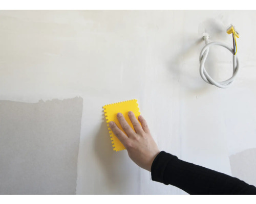 Hand mit gelbem Werkzeug zum Glätten einer Wand.