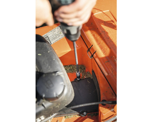 Une personne utilise un tournevis pour réparer une tondeuse à gazon.