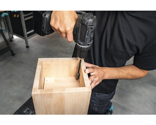 Un artisan visse un meuble en bois à l''aide d''une perceuse sans fil