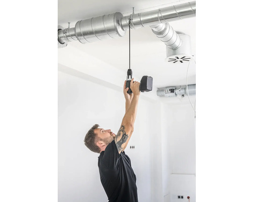 Un homme fixe un conduit de ventilation au plafond à l''aide d''une perceuse sans fil.