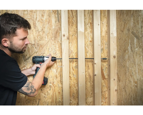 Un homme visse des lattes en bois sur un panneau de particules à l''aide d''une visseuse sans fil