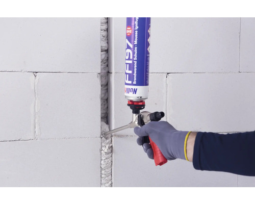 Un artisan remplit un joint dans un mur en béton cellulaire avec une mousse expansive.
