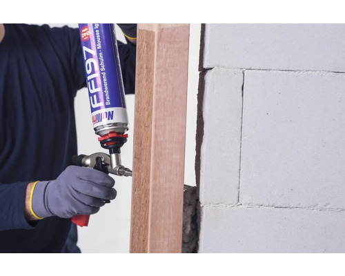 Un artisan utilise de la mousse ignifuge pour sceller un cadre en bois sur un mur.
