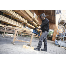 Homme avec visière de protection coupant du bois avec une scie Bosch