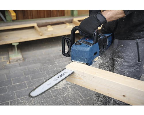 Une personne scie une planche de bois avec une tronçonneuse à batterie Bosch.