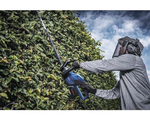 Homme avec visière de protection taillant une haie avec un taille-haie sans fil