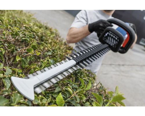 Une personne taille une haie avec un taille-haie.