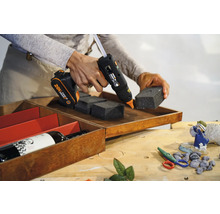 Pistolet à colle sans fil fixant des pièces en mousse dans une boîte en bois.