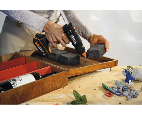 Pistolet à colle sans fil fixant des pièces en mousse dans une boîte en bois.