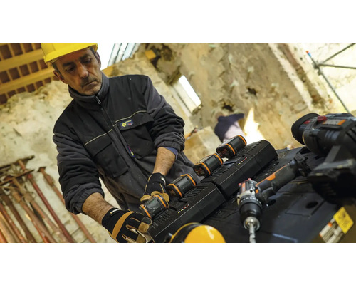 Ein Bauarbeiter mit Schutzhelm wechselt den Akku eines Elektrowerkzeugs auf einer Baustelle.