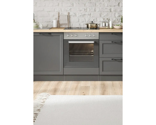 Scène de cuisine avec armoires grises, cuisinière, four et plan de travail en bois devant un mur de pierre