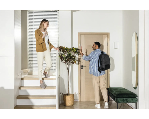 Hall d''entrée lumineux avec escalier, vestiaire et deux personnes qui se disent au revoir.
