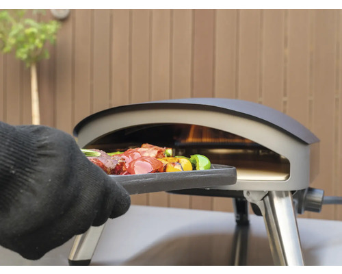 Ein Grillofen mit Grillgut wird mit einem Handschuh bedient.