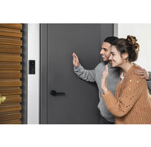Un couple fait signe de la main devant une porte d''entrée avec une sonnette vidéo installée.