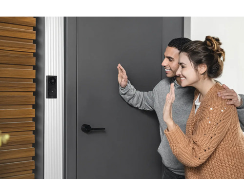 Un couple fait signe de la main devant une porte d''entrée avec une sonnette vidéo installée.