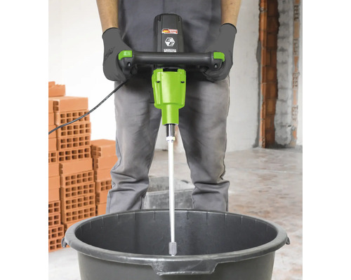 Un homme utilise un mélangeur à mortier dans un seau sur un chantier de construction.