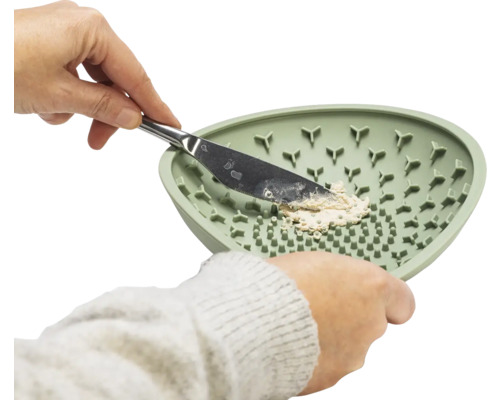 Une main tient une spatule dans un bol à mélanger vert texturé pour mélanger une pâte.