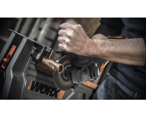 Eine Person schneidet mit einem Trennschleifer ein Kupferrohr, das in einer Werkbank befestigt ist. WORX Logo.