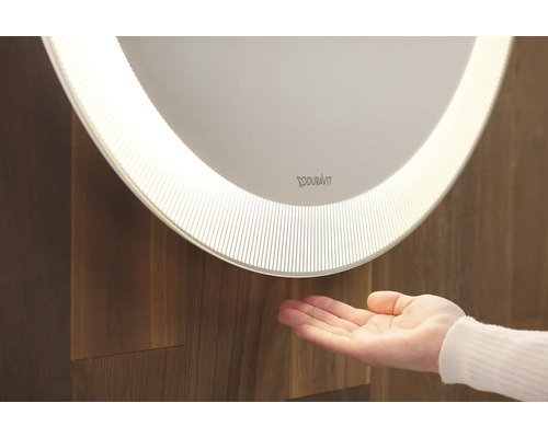 Miroir Duravit éclairé avec main devant un mur en bois