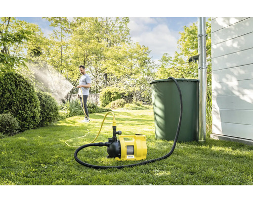 Jardin avec récupérateur d''eau de pluie, pompe domestique et personne arrosant les plantes