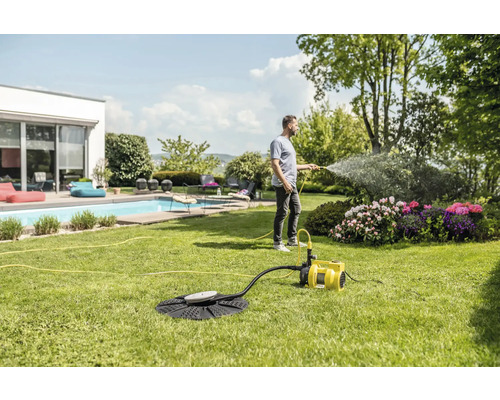 Un homme arrose un jardin avec une pompe de jardin à côté d''une piscine.