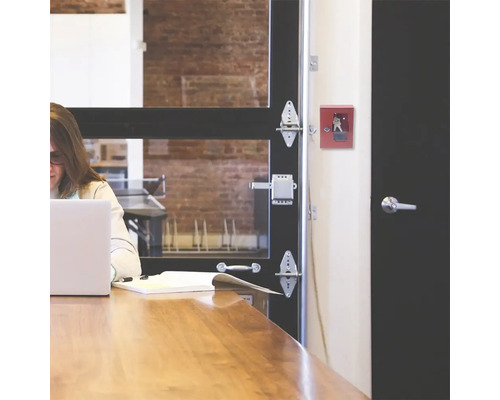 Scène d''un bureau avec un coffre-fort à clés rouge au mur, une table en bois et une femme travaillant sur un ordinateur portable.
