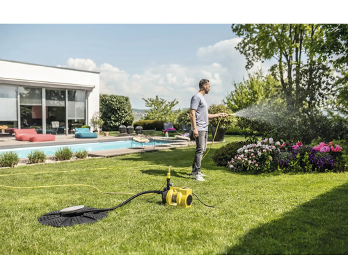 Ein Mann bewässert mit einer Gartenpumpe den Garten.