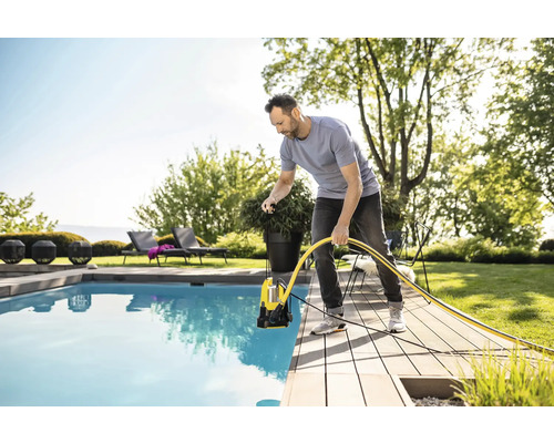Un homme utilise une pompe submersible pour pomper l''eau d''une piscine. On aperçoit du mobilier de jardin à l''arrière-plan.