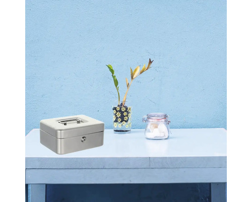 Coffre-fort en métal avec clé, vase avec plantes et verre sur une table