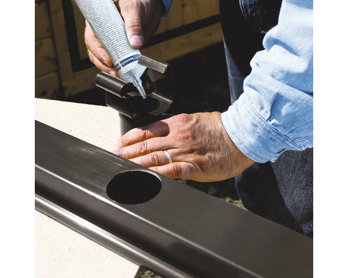 Personne appliquant du mastic d''étanchéité sur un tuyau de descente pluviale pour gouttière