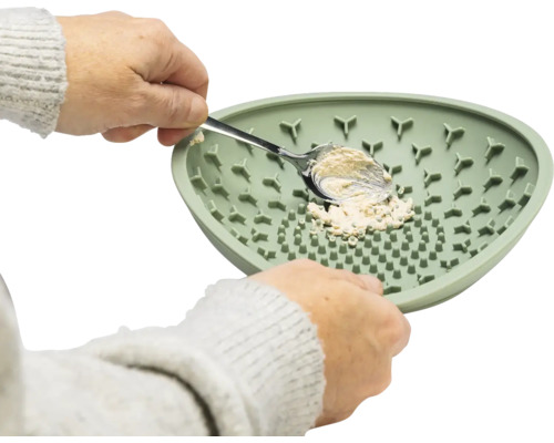 Une personne racle de la matière avec une cuillère d''une assiette verte en silicone.