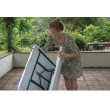 Eine Frau klappt einen Klapptisch im Garten zusammen.