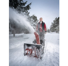 Un homme utilise une souffleuse à neige pour déneiger une route enneigée