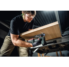 Un homme scie une plaque de bois avec une scie sauteuse sans fil Metabo sur un établi