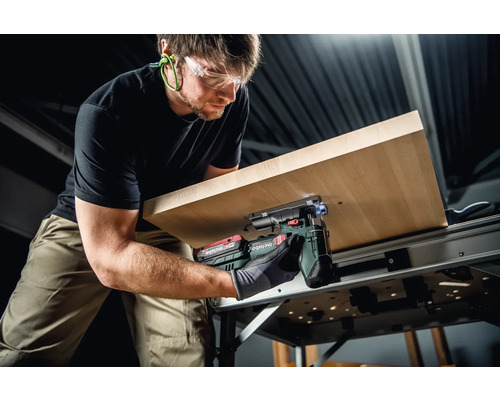 Un homme scie une plaque de bois avec une scie sauteuse sans fil Metabo sur un établi